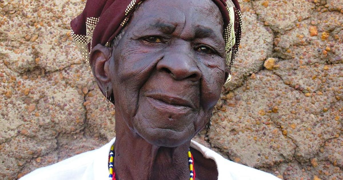 Elderly African woman wearing headscarf, portrait against textured wall outdoors in Fada-Ngourma, Burkina Faso.