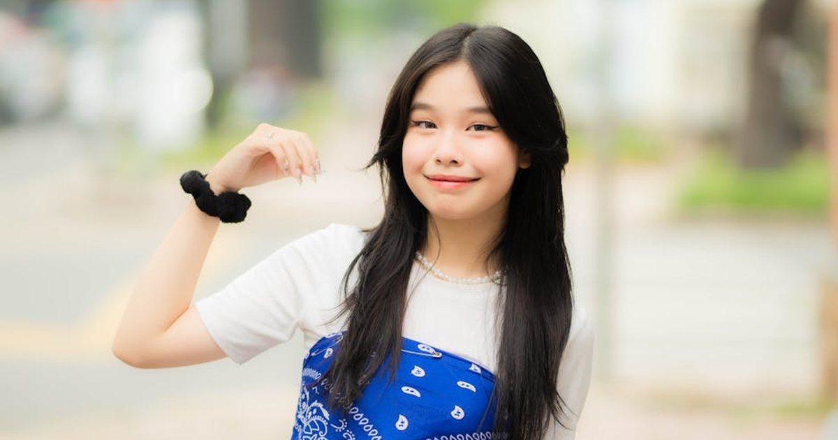A young, smiling woman poses outdoors with a blue scarf, exuding charm and confidence.