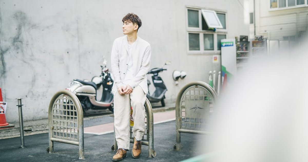 Asian man wearing white suit sitting on a sidewalk with motorbikes in the background.