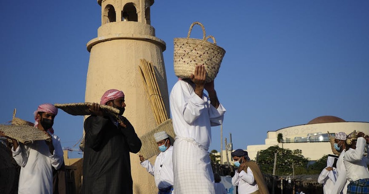 Arab men carrying baskets near a traditional building in Doha, Qatar.