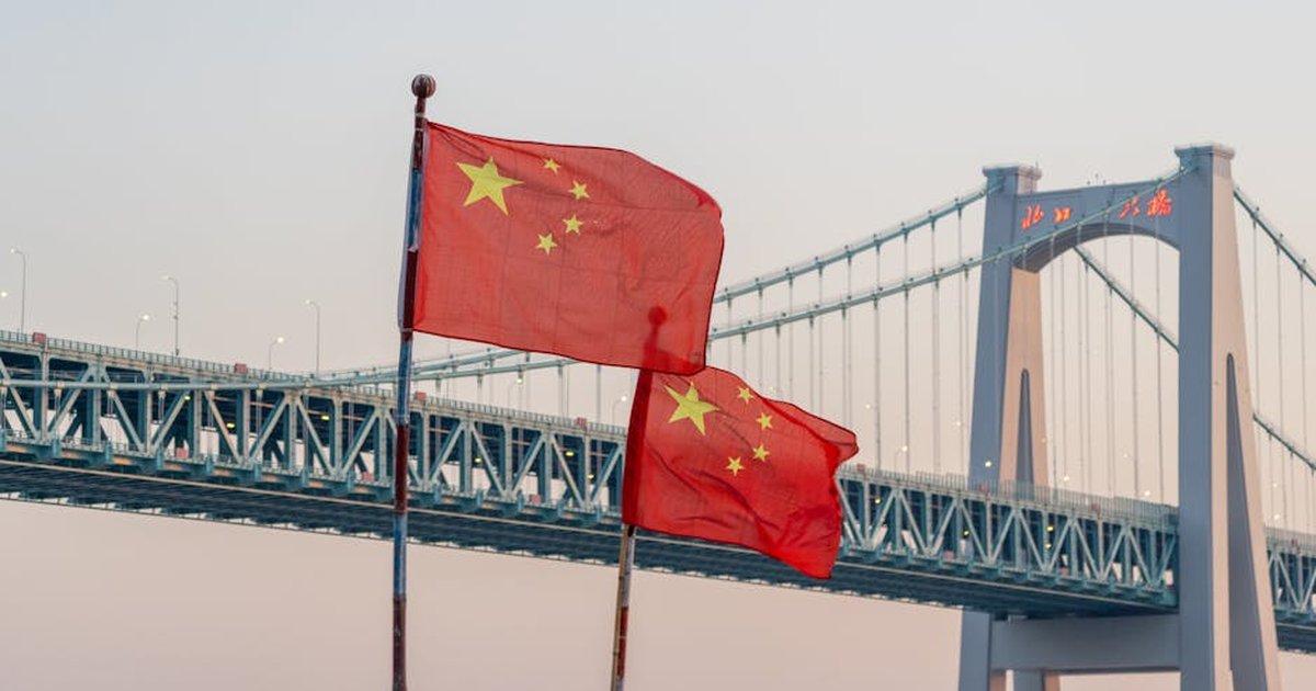 Chinese flags waving in front of a bridge at sunset, showcasing national pride and architecture.