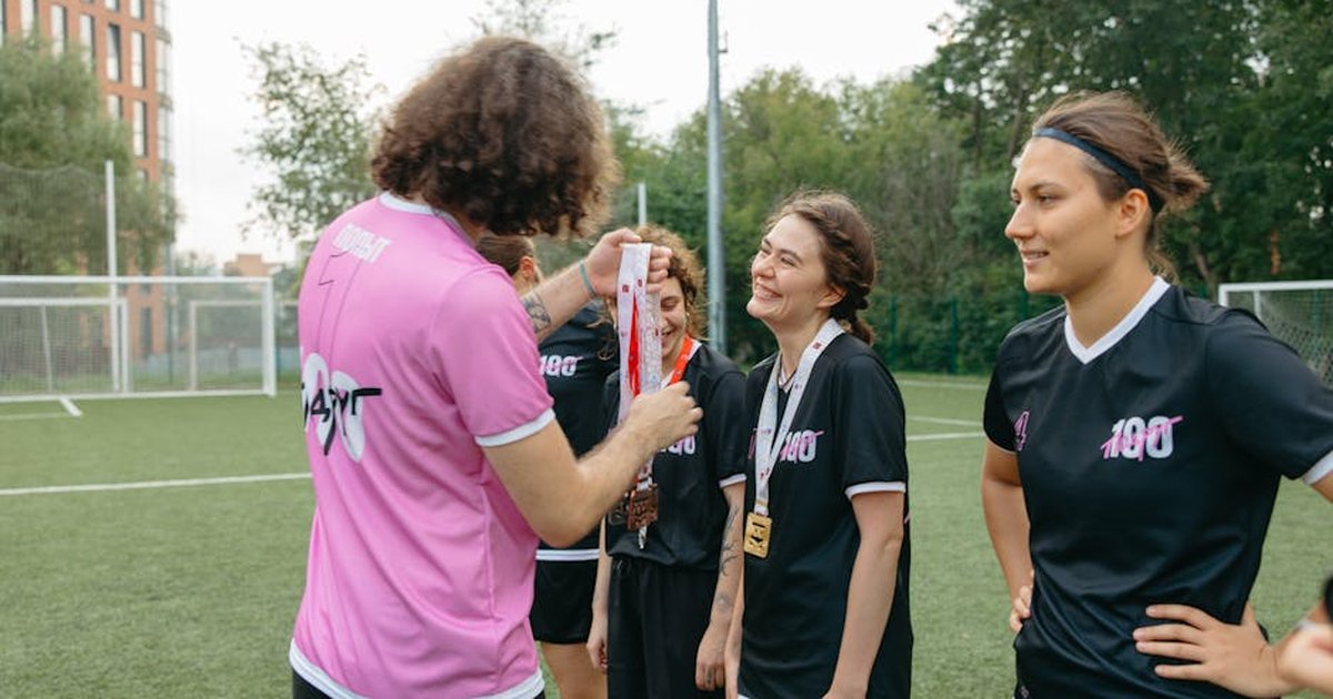 A women's football team receiving medals on the field, celebrating their victory.