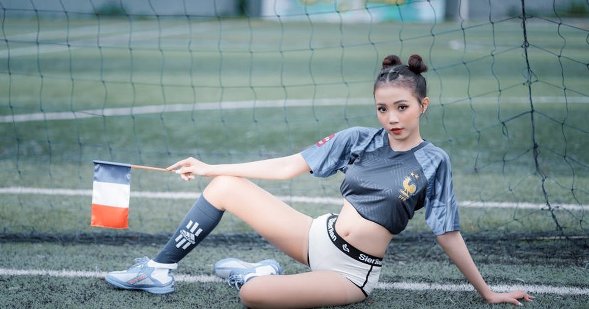 Young woman on soccer pitch holding a flag, blending fashion and sports with vibrant energy.