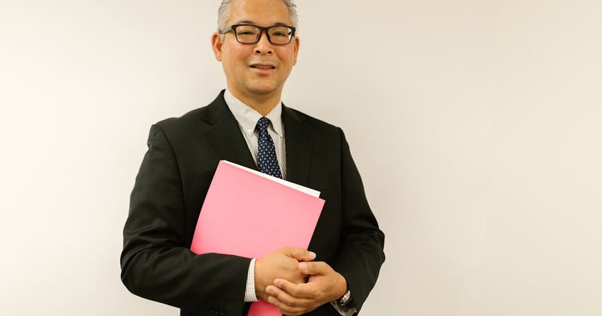 Confident businessman in black suit holding pink folder, smiling at the camera indoors.
