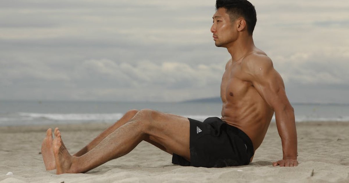 Fit young man sitting on a beach, enjoying a serene moment at the seaside.
