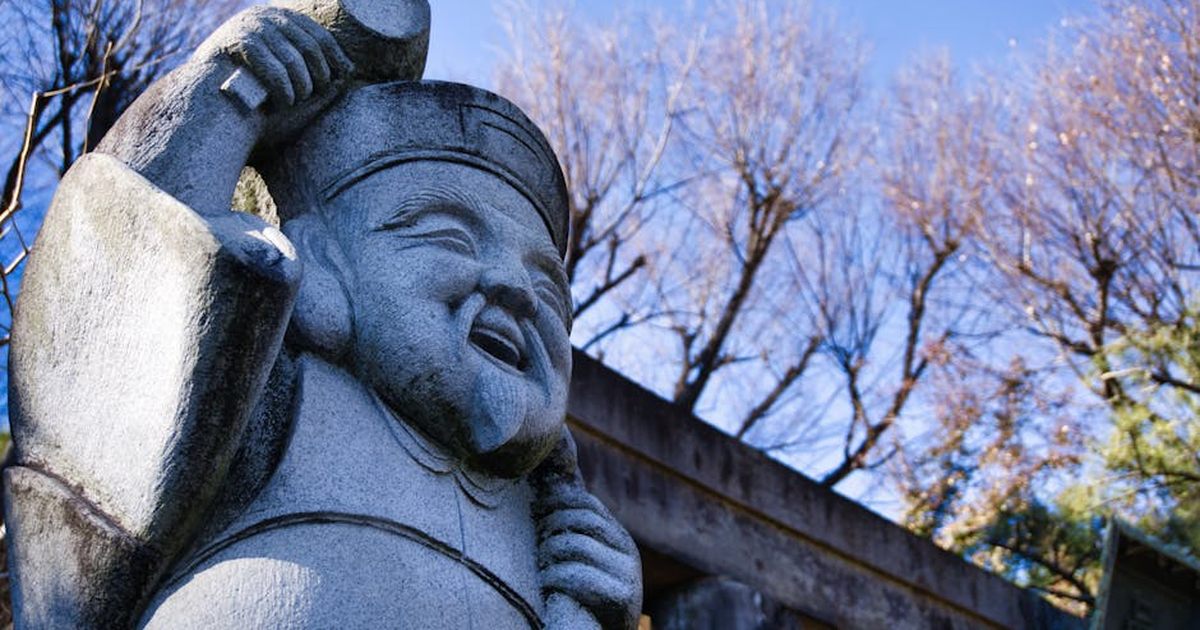 Statue of Daikoku Sama in Shinagawa Ward, Tokyo under a clear blue sky next to bare trees.