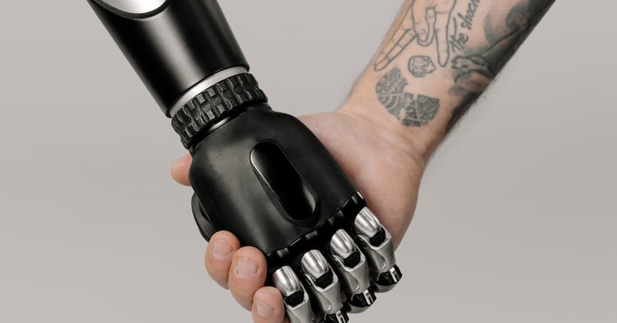 Tattooed human hand holding a prosthetic hand in a studio setting, symbolizing connection and technology.