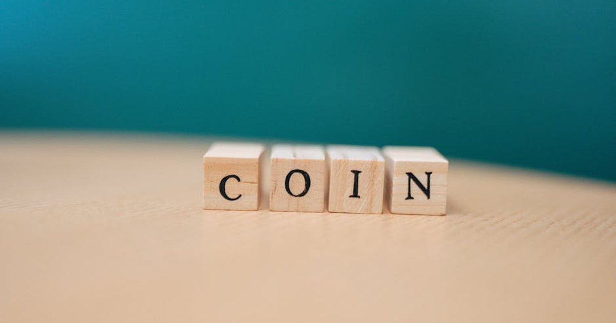 Wooden blocks arranged to spell 'coin' on a wooden surface against a teal background.