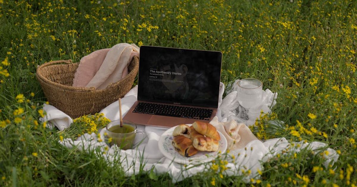 Serene outdoor picnic setup with MacBook Air, pastries, and matcha drink surrounded by blooming spring flowers.