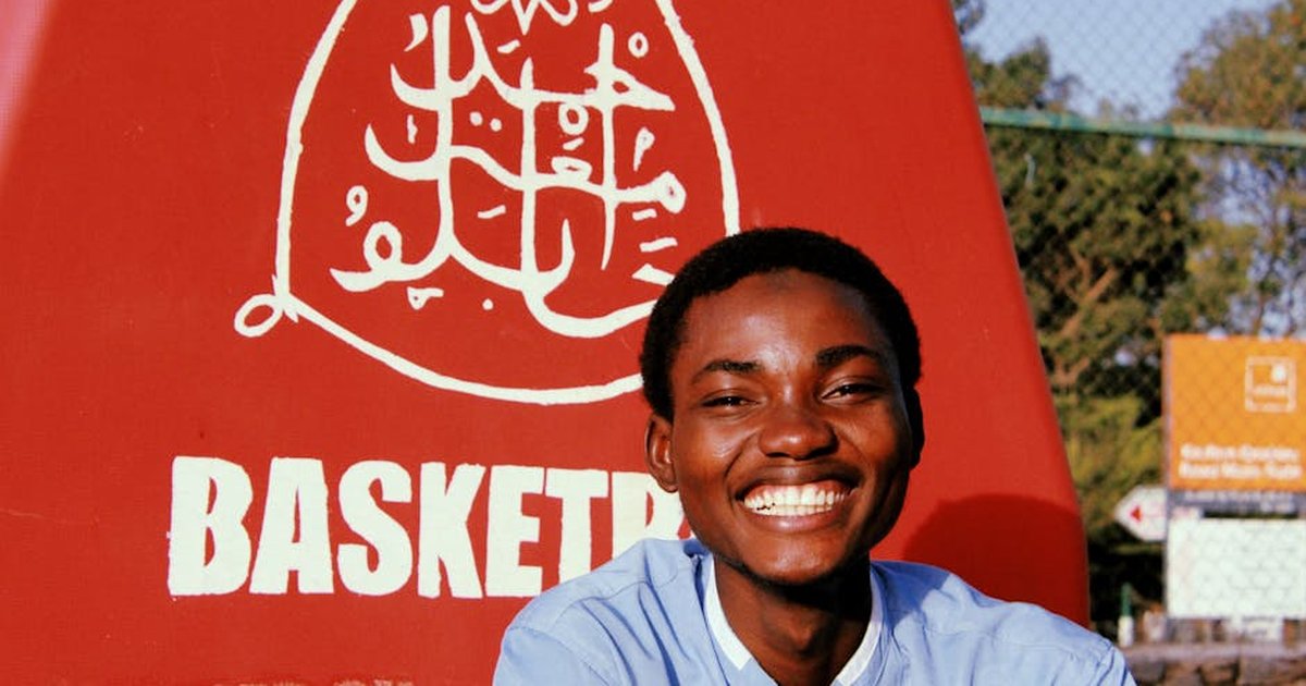 A cheerful young man smiling broadly at an outdoor basketball court, showcasing joy and positivity.