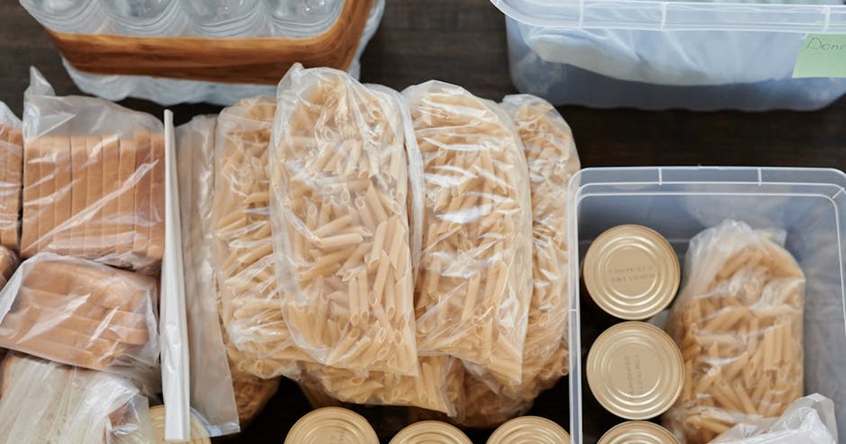 Aerial shot of pantry essentials including pasta, canned food, and bread packaged in plastic bags.