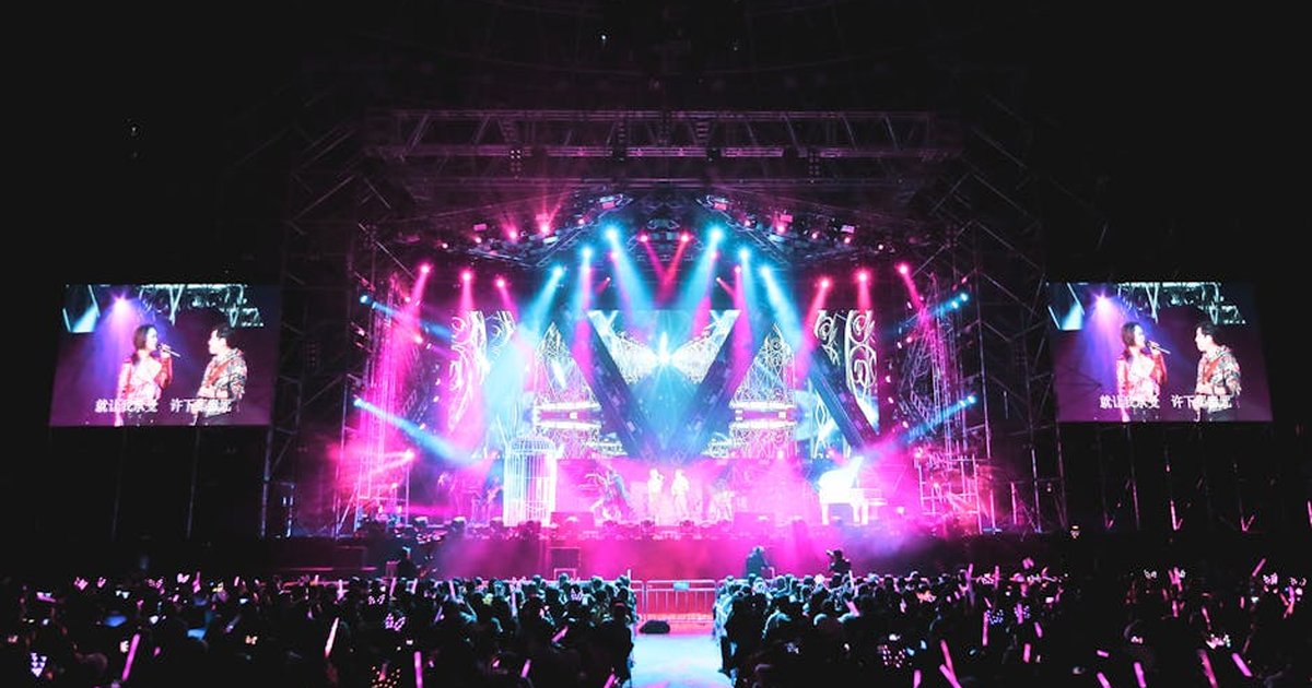 Anonymous artists with microphones giving performance on platform illuminated by colorful spotlights in concert hall with audience at night