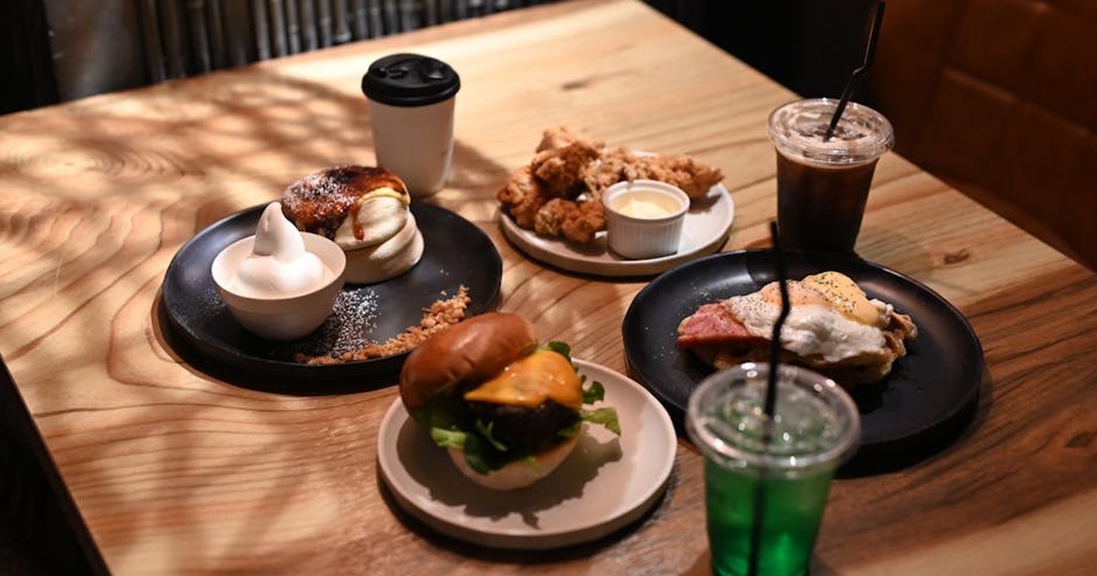 A cozy dining scene featuring burgers, fried chicken, and drinks on a wooden table with sunlight filtering in.
