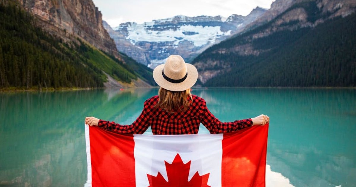 Woman holding a Canadian flag at stunning Lake Louise, Alberta, embracing nature and patriotism.
