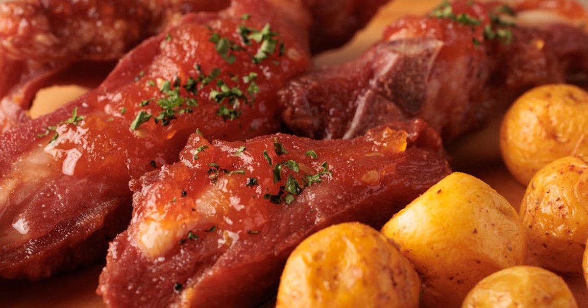 Close-up of juicy Colombian pork ribs with herbs and roasted potatoes.