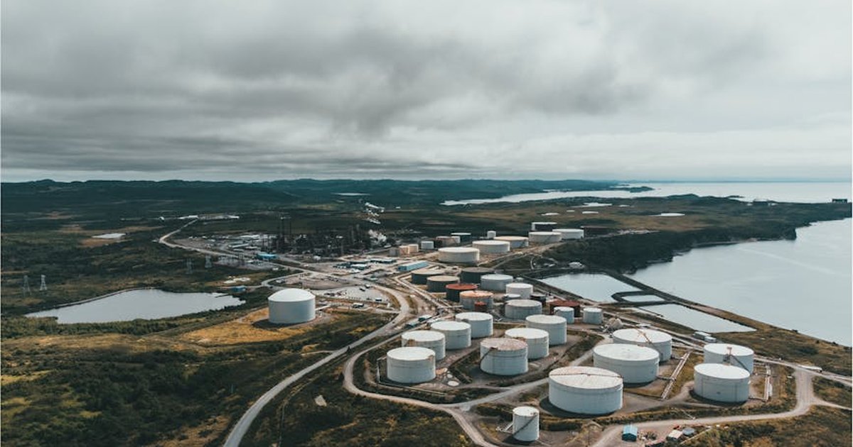 Aerial landscape shot of a coastal oil refinery with storage silos under cloudy skies.