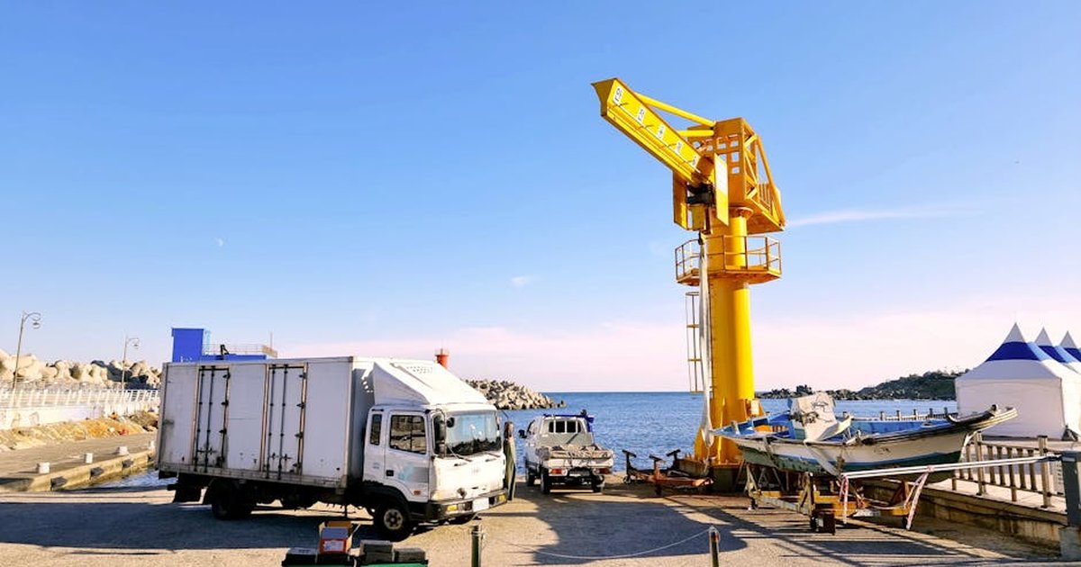 Colorful harbor scene in Busan featuring a yellow crane, trucks, and sea view.
