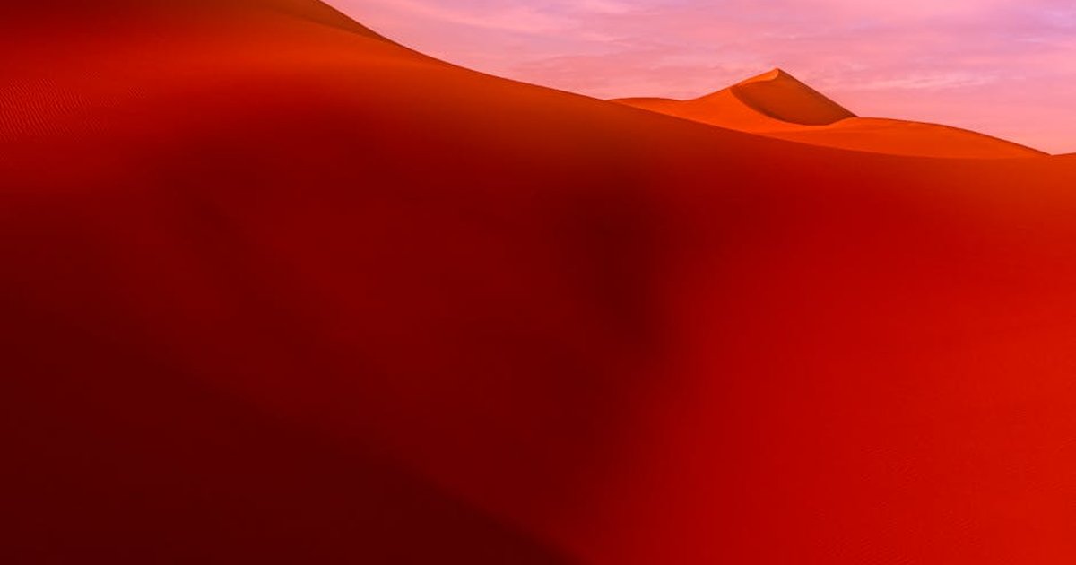 A captivating view of red sand dunes with a soft pink sky at sunset, showcasing nature's beauty.