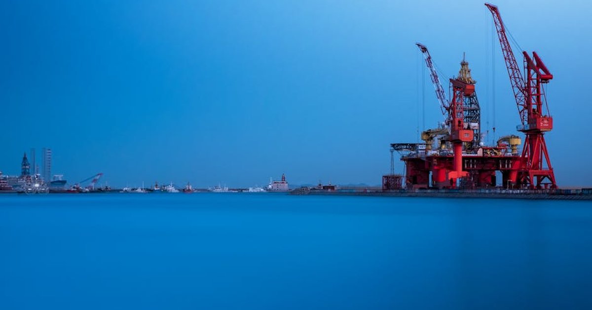 A vibrant offshore oil rig with large cranes at a busy sea port during the day.