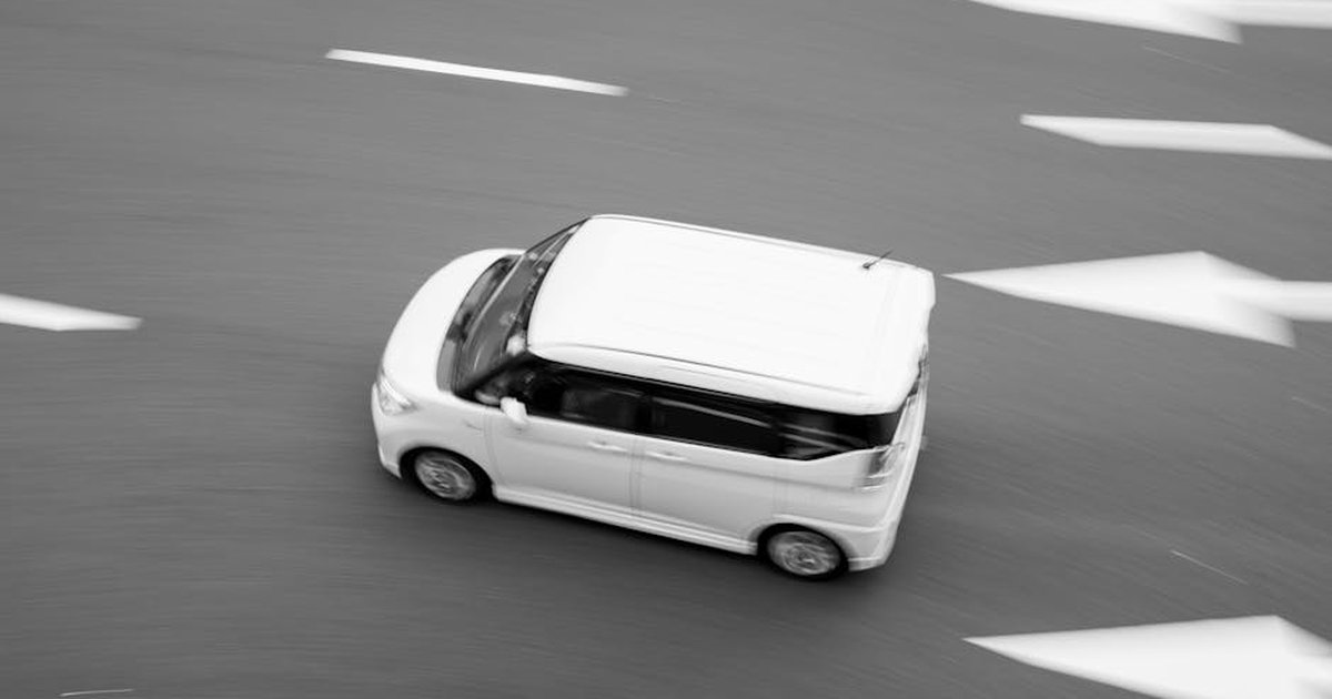 Black and white photo of a moving car on a road with directional arrows, emphasizing motion.