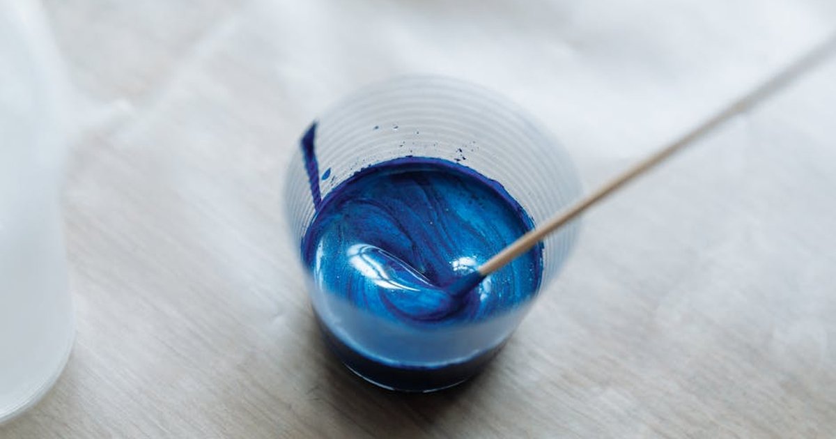 Close-up of vibrant blue paint being mixed in a clear plastic cup with a wooden stick.