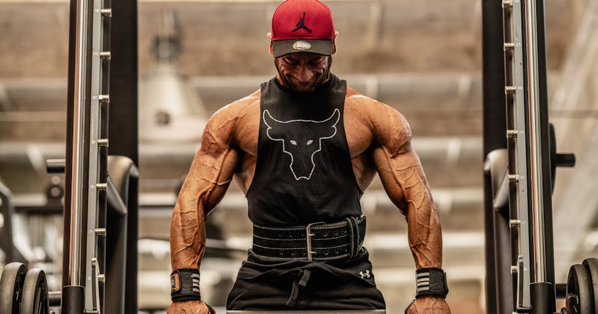 A strong, muscular man in a gym lifting a barbell, showcasing intense focus and strength.