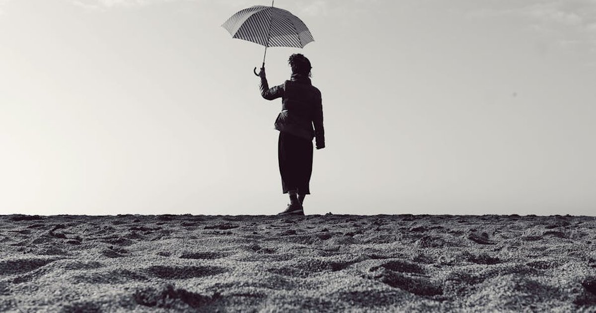 Black and white silhouette of a woman holding an umbrella while standing on a serene beach.