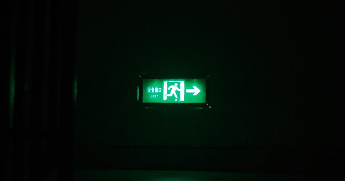 Illuminated green exit sign with directional arrow in a dark indoor setting.
