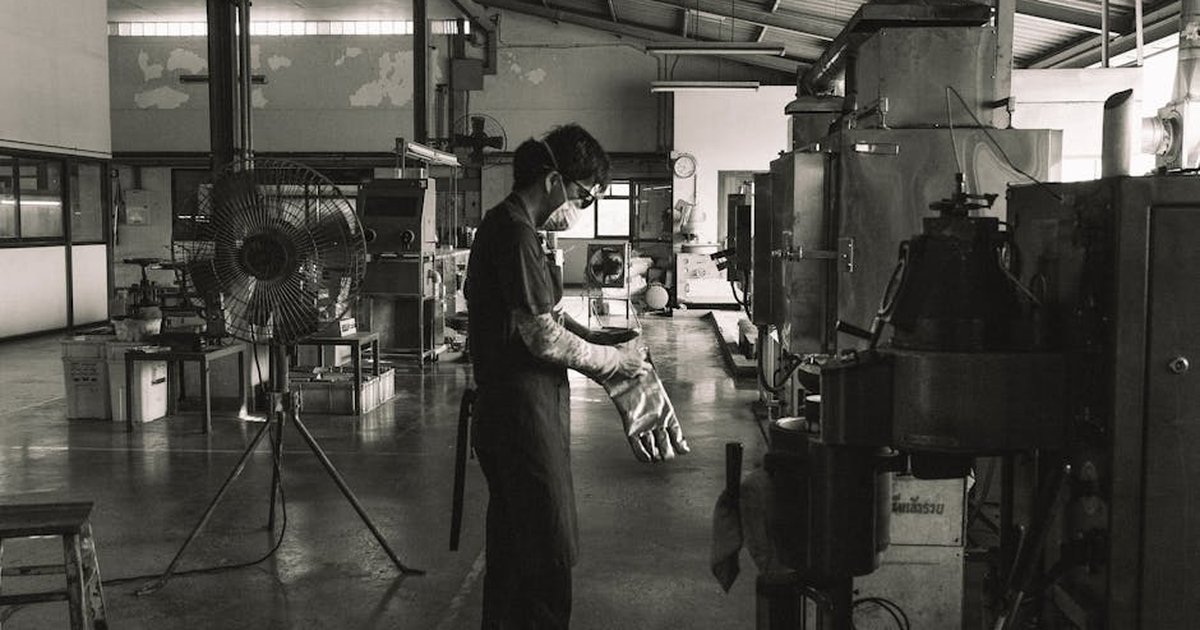 A masked worker operating machinery in a Bangkok factory, showcasing industrial safety.