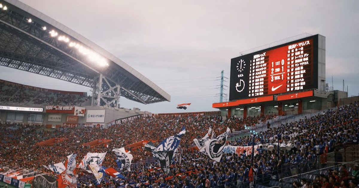 A lively soccer stadium scene with fans waving flags and a scoreboard displaying match details.