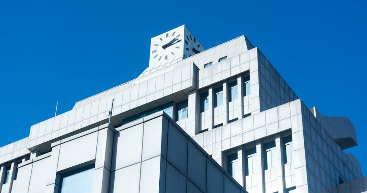 Sleek modern building with a clock tower against a vibrant blue sky, highlighting minimalistic design.