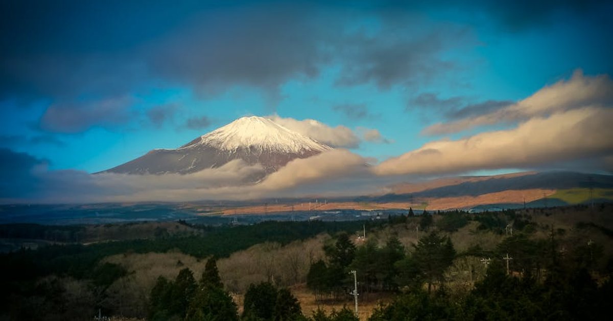 A breathtaking view of Mount Fuji with a snow-capped peak, surrounded by clouds and serene nature.