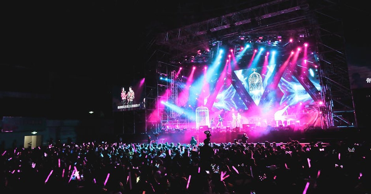 Unrecognizable musicians performing on concert hall stage illuminated by colorful spotlights in front of public in evening