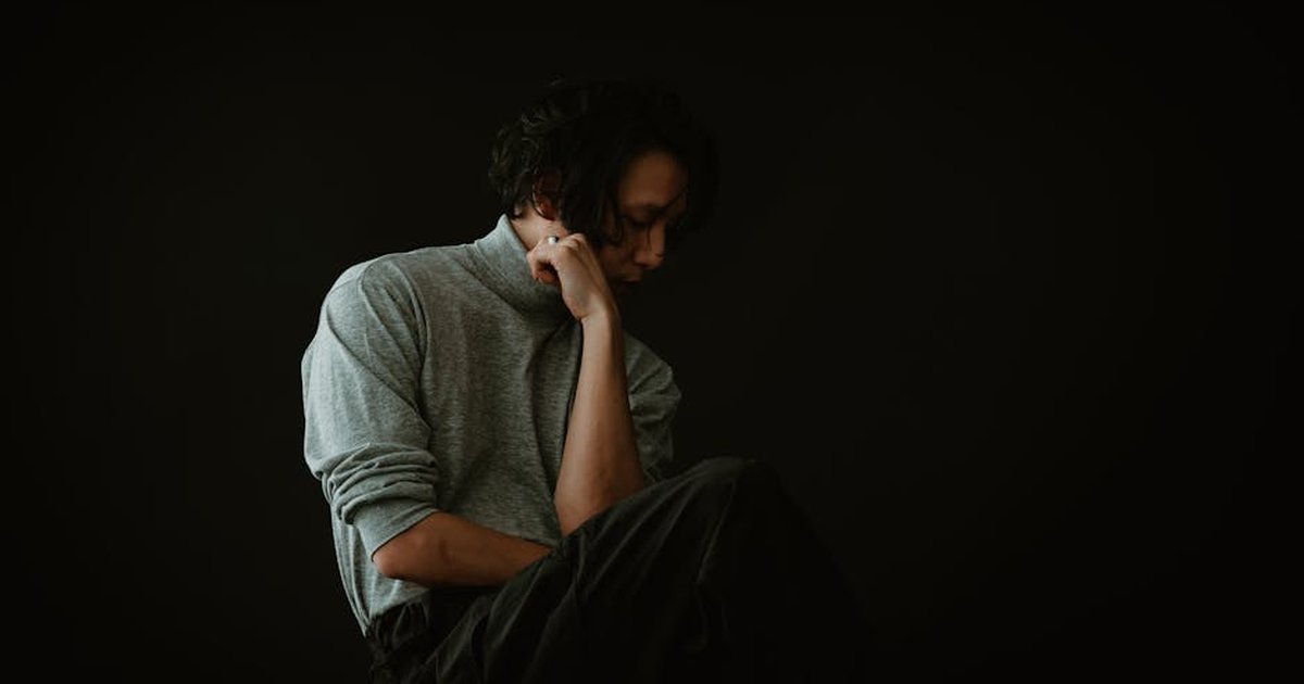Artistic portrait of an Asian man in a thoughtful pose against a black background.