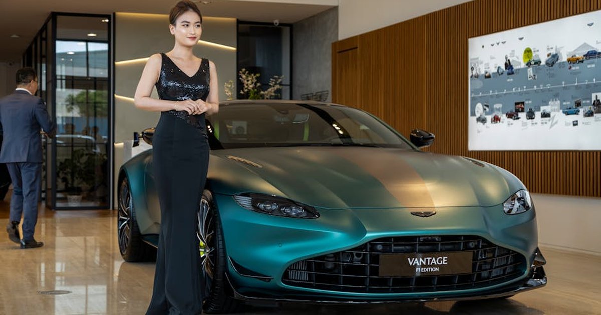 Asian woman posing with Aston Martin Vantage in a luxury showroom setting.