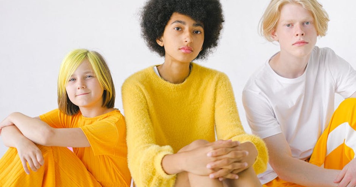 Diverse teenagers in bright yellow outfits with dyed hair and Afro hairstyle looking at camera on white background