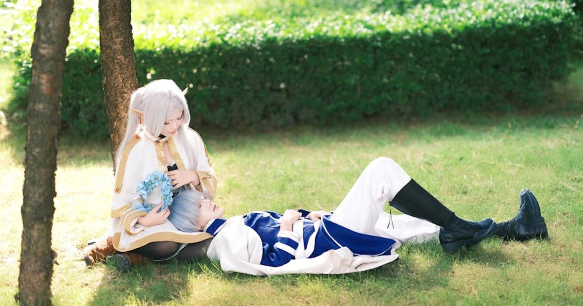 Two fantasy cosplay characters relaxing on grass, showcasing creativity and costume artistry.