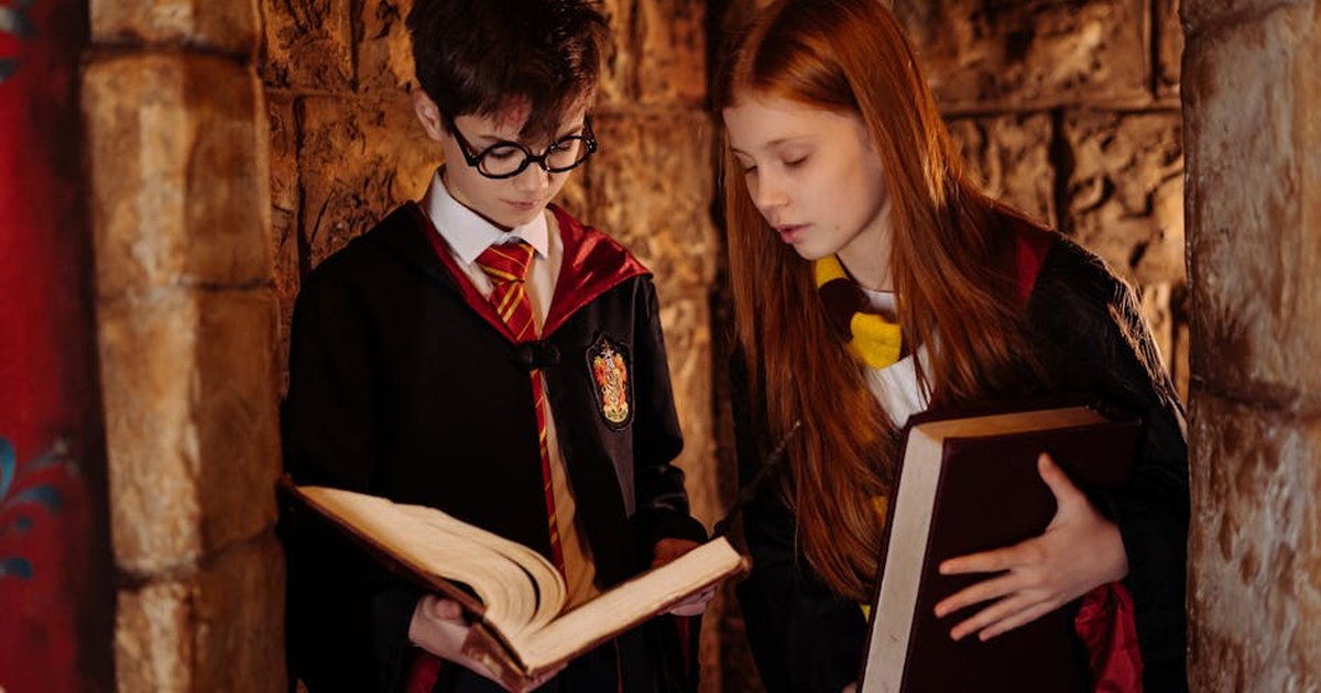 Two children in wizard costumes reading in a stone-walled corridor.