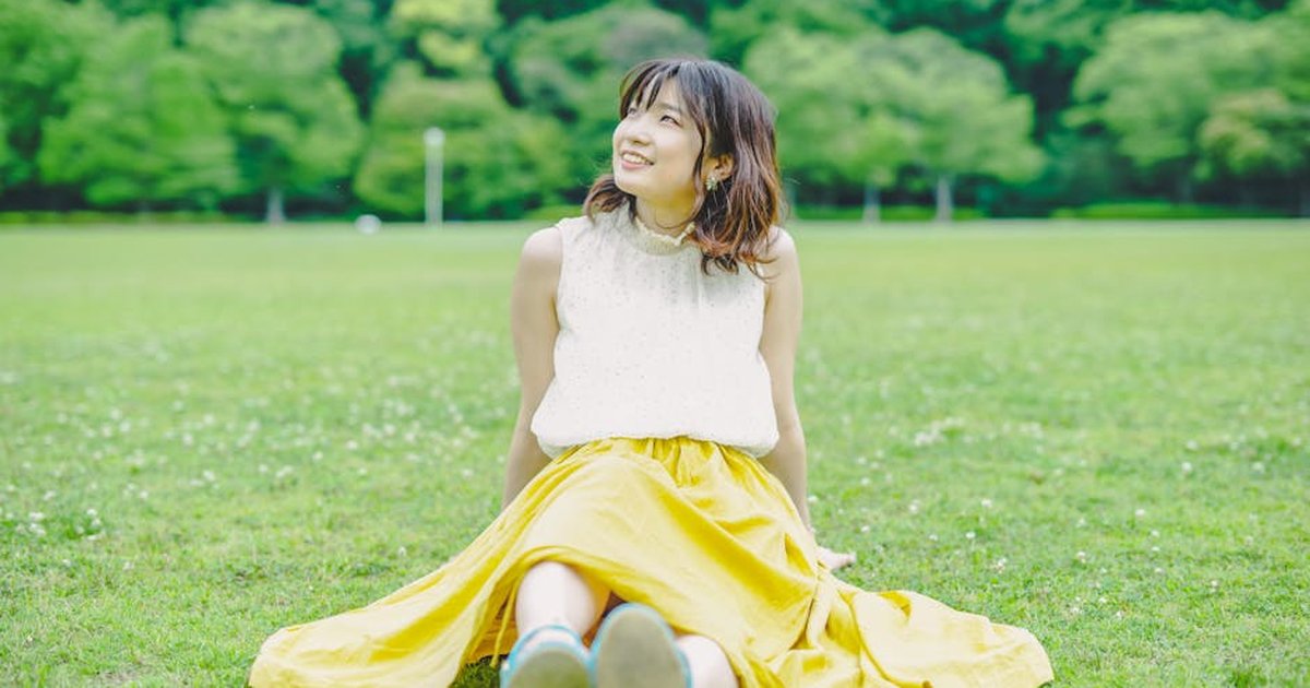 Smiling young woman sitting on grass in a park, enjoying a sunny day.