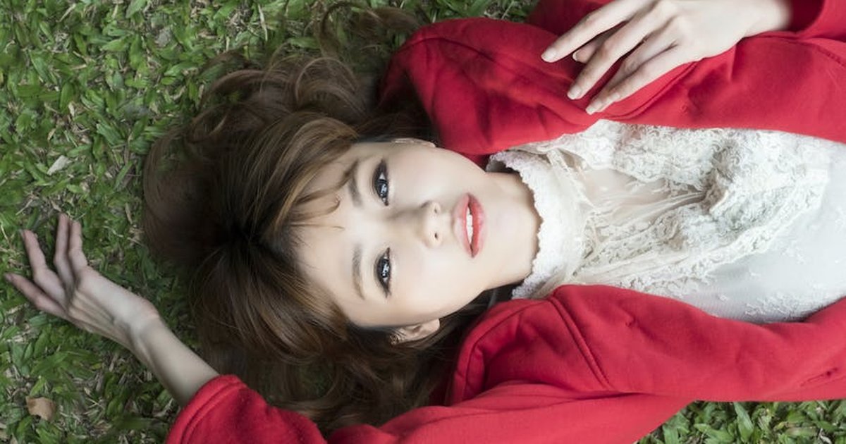 A young woman with a red jacket lying on green grass, serene and stylish.