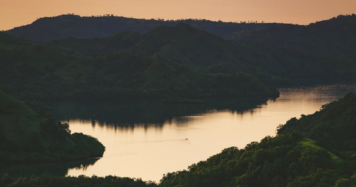 A tranquil sunset view over a lake with reflections and lush hills in Indonesia.