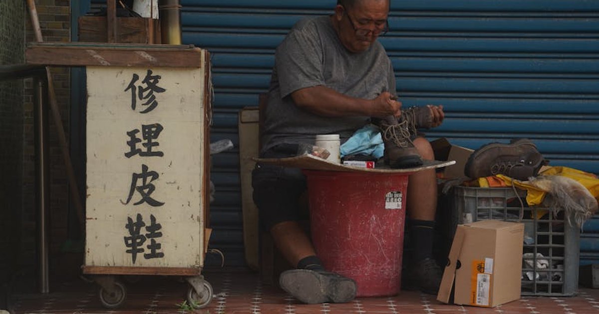 Elderly man repairing shoes on a Taiwan city sidewalk. Urban candid scene.