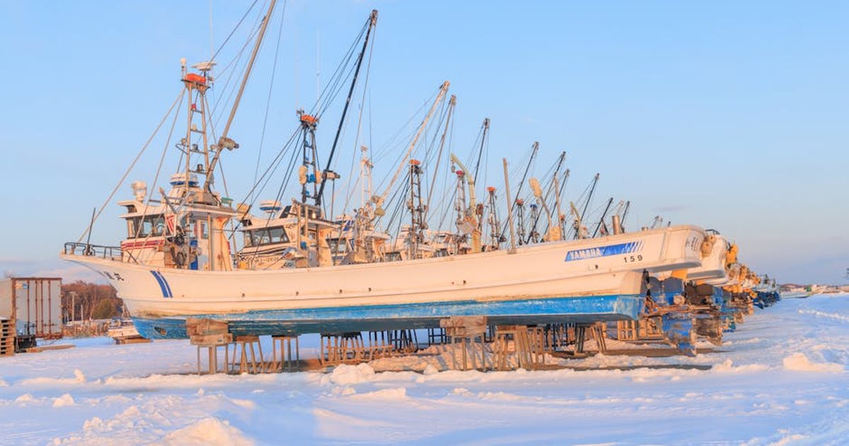 Fishing boats on snowy shore in Hokkaido, Japan during winter sunlight.