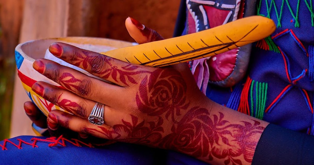 Detailed close-up of henna-adorned hands holding a colorful calabash bowl in Kaduna, Nigeria.