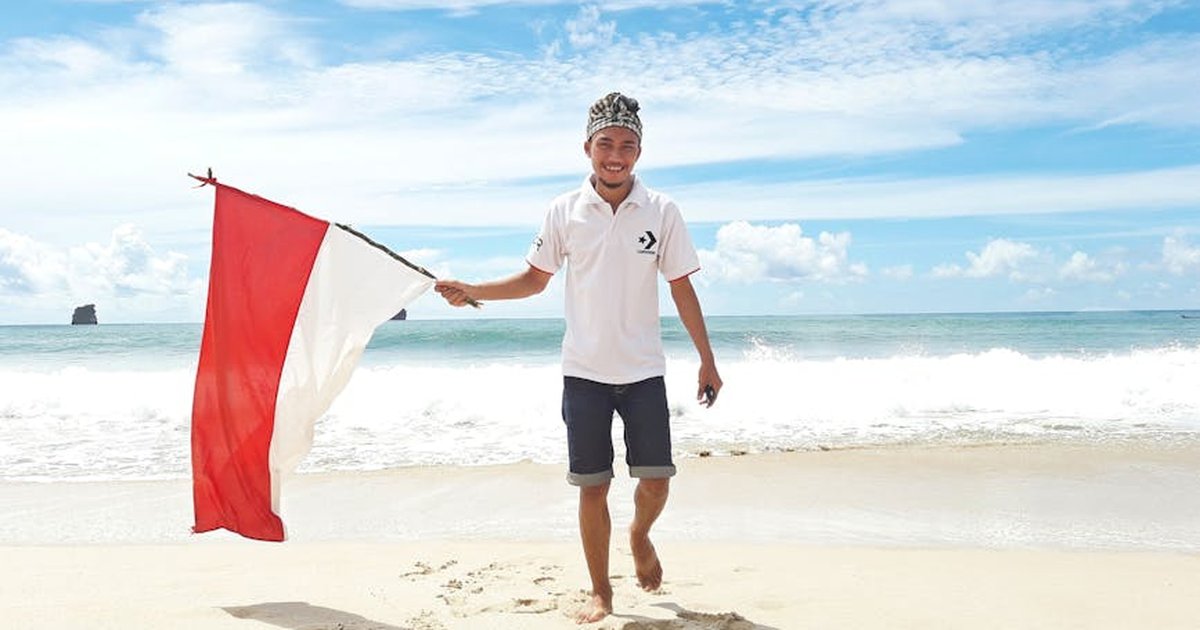 Happy man on a sunny beach holding the Indonesian flag, symbolizing freedom and adventure.