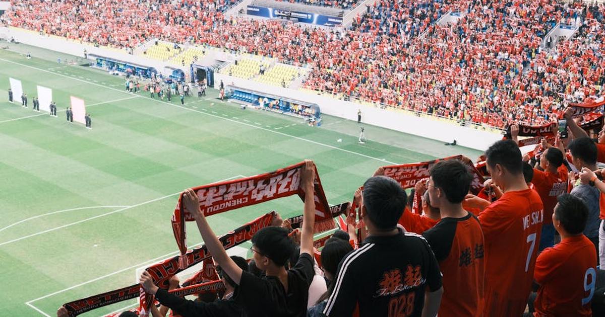 Crowd of soccer supporters in a stadium, waving scarves and cheering during a lively match.