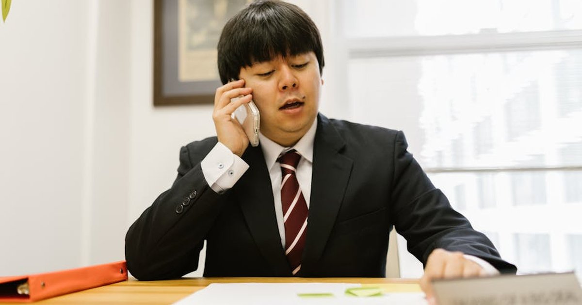 Asian businessman in black suit talking on phone at desk in office