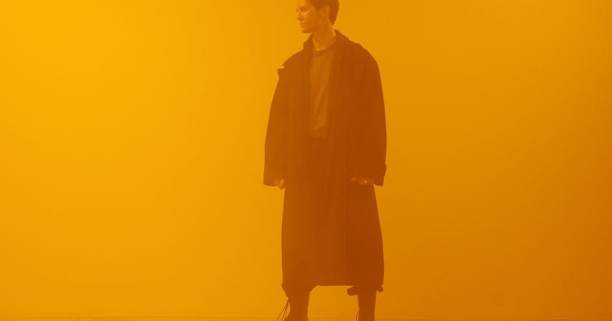 Man in black coat standing against an orange background, embodying a cyberpunk retro-futuristic style.