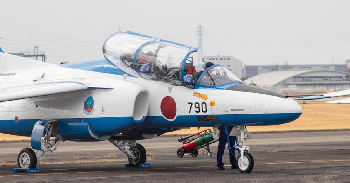 Training jet with Japanese insignia taxiing for preparation on airfield.