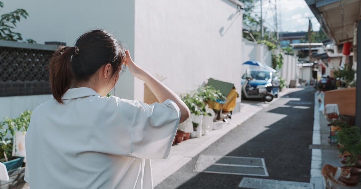 A woman walks through a sunlit alley in an urban area, shielding her eyes.